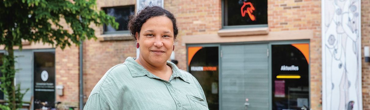 Eine Frau mit dunklen Haaren, gekleidet in grüngrauer Bluse, steht vor dem Frauenzentrum in der Schiffbauergasse