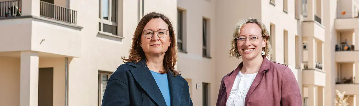 Zwei weibliche Personen stehen vor einem Neubauensemble mit Balkonen