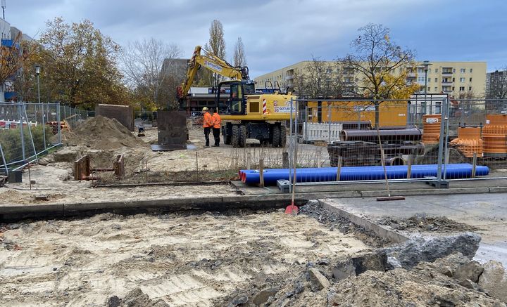 Baustelle mit blauen Leitungsarbeiten und Bauarbeite sowie Maschinen im Hintergrund