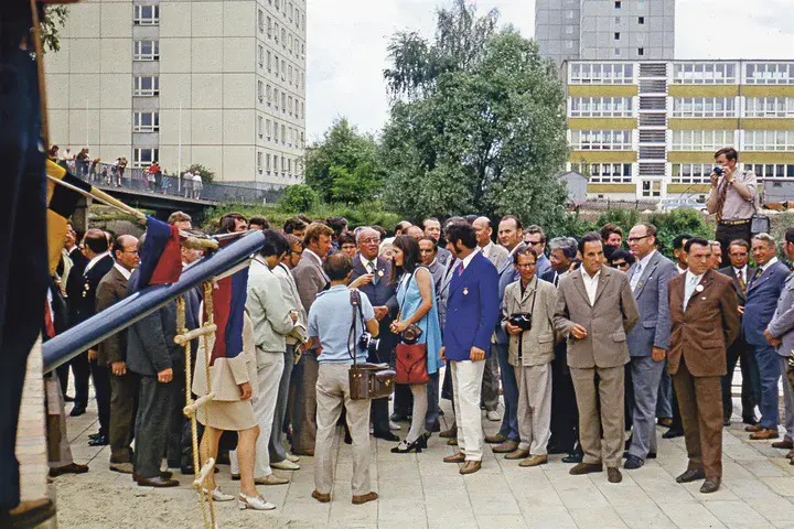 Im Mittelpunkt: Hiltrud Berndt auf der Freundschaftsinsel, 1973. Viele Menschen stehen auf einem Platz, im Hintergrund sind Häsuer (Plattenbauten) zu erkennen.