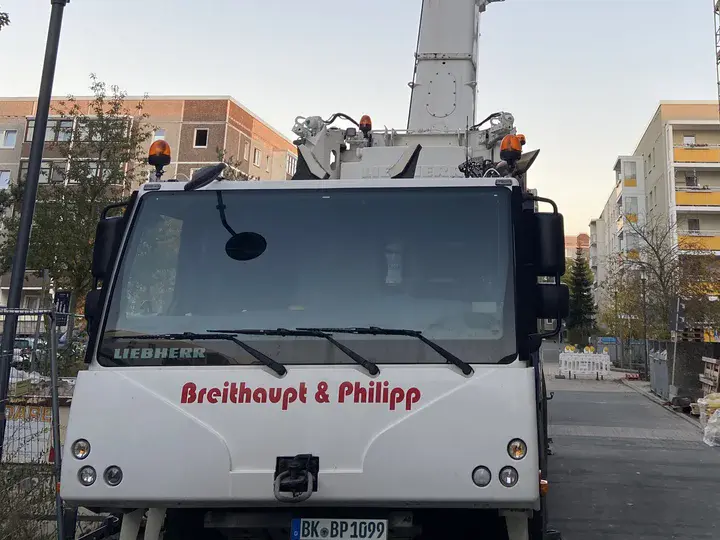 Weißes Baufahrzeug neben einer Baustelle.