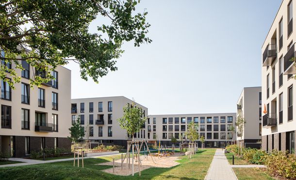 Innenhof mit Spielplatz, Rasen und Wegen der neu gebauten Wohnanlage mit Blick auf fünf mehrstöckige, moderne Häuser