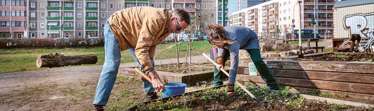 Ein Mann und eine Frau machen Gartenarbeit, im Hintergrund stehen Plattenbauten