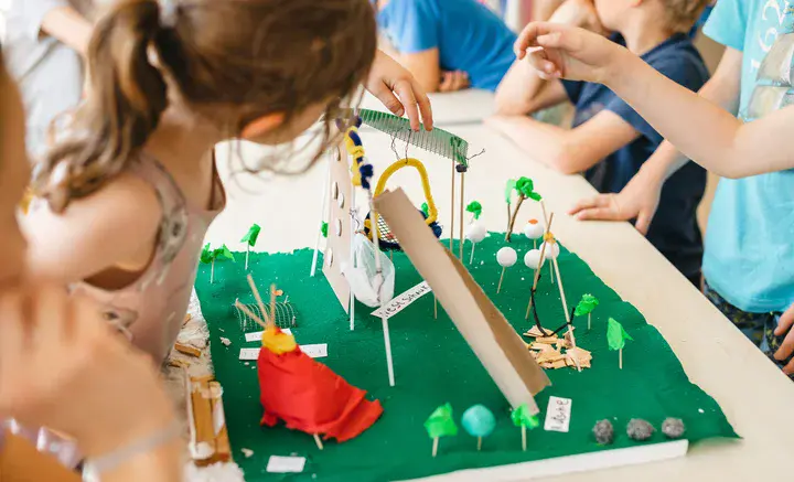 Kinder betrachten und gestalten gemeinsam ein detailreiches Modell eines Spielplatzes auf einem Tisch.