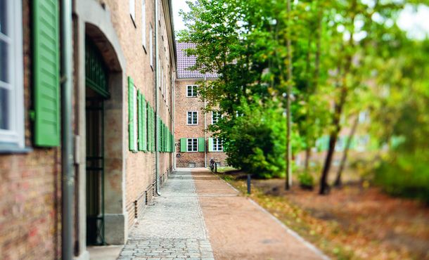 helle Backsteine und grüne Fensterläden sowie hoher Baumbewuchs zeigen den Charme der sanierten Altbausiedlung