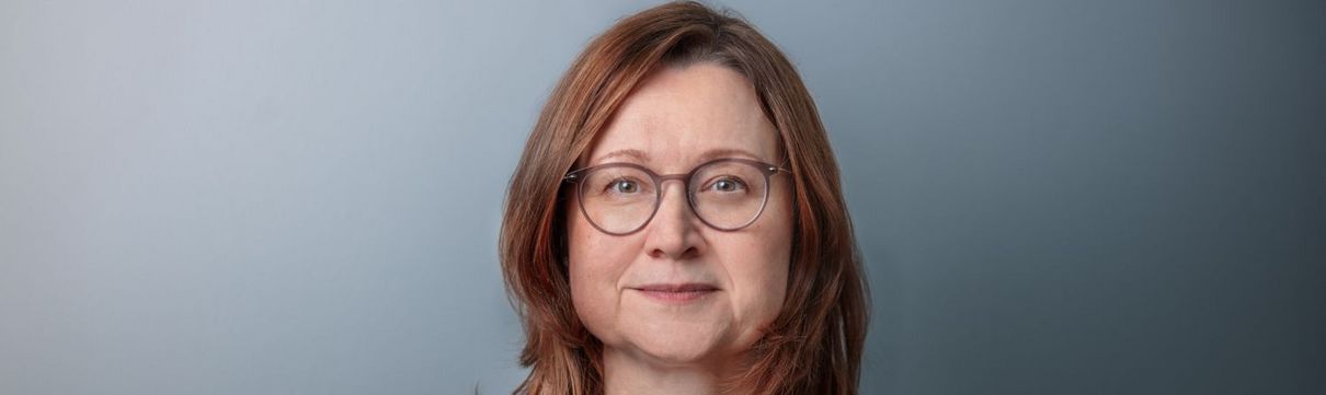 Portrait von Sandra Jacob, Geschäftsführerin Luftschiffhafen Potsdam GmbH, vor graublauem Hintergrund.