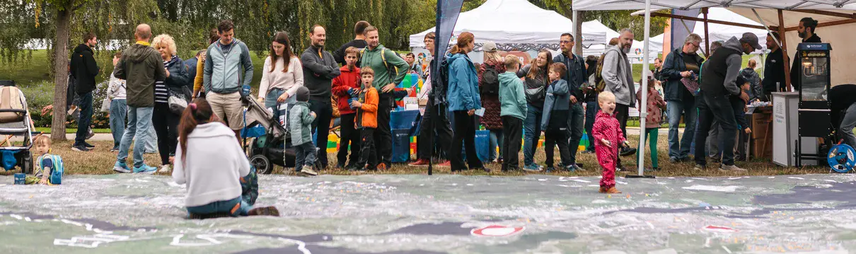 Besucherinnen und Besucher an Informationsständen bei einem Familienfest im Park vor großem Stadtplan.