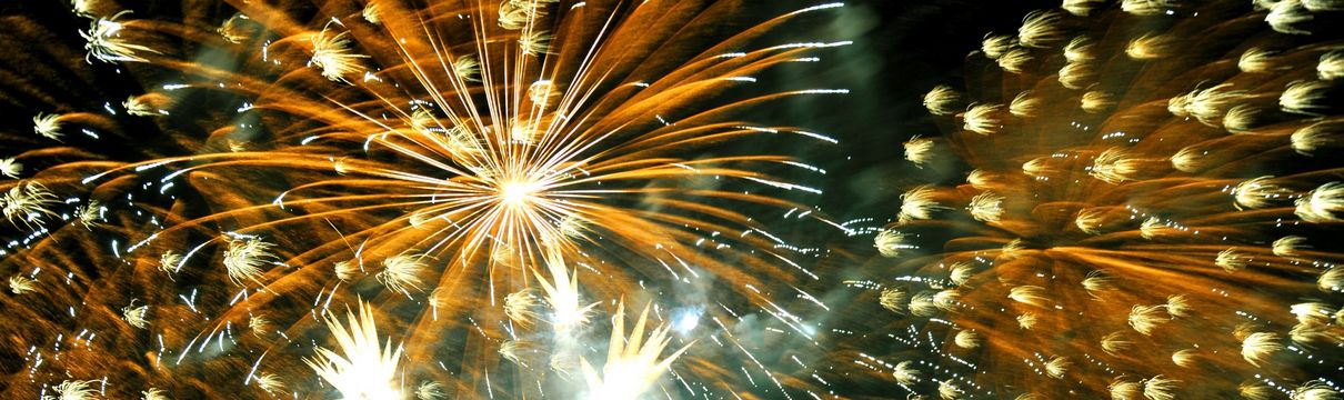 Bunte Feuerwerksexplosionen und Menschen, die in den Himmel schauen.