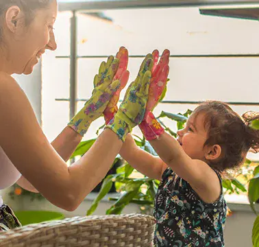 Eine Mutter und ihr Kind tragen bunte Handschuhe und drücken lachend ihre Handflächen aneinander