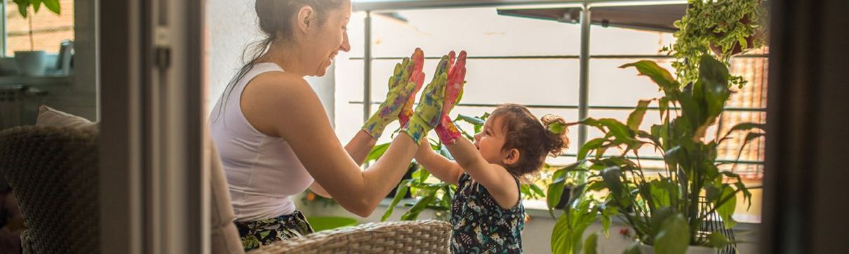 Eine Mutter und ihr Kind tragen bunte Handschuhe und drücken lachend ihre Handflächen aneinander