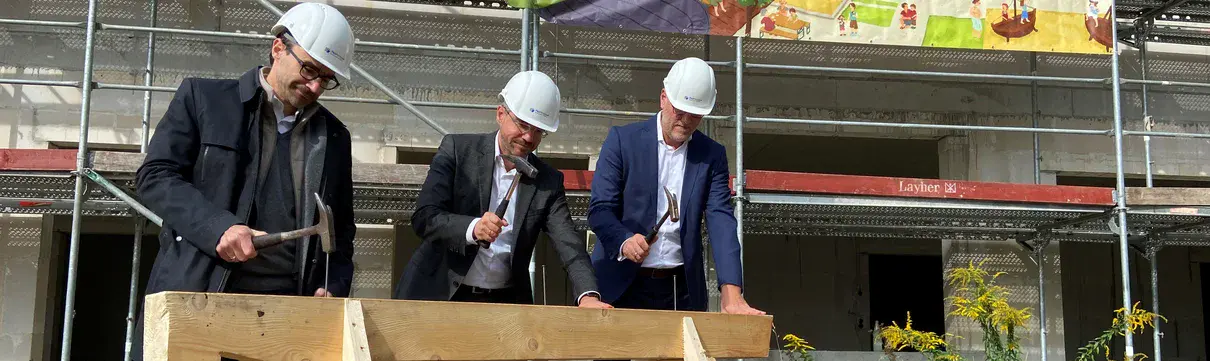 Richtfest Kita Hermann-Mattern-Promenade (Foto Sebastian Brandner) Vertreter der ProPotsdam und der Oberbürgermeister der Stadt stehen vor einem neu errichteten Gebäude und schlagen Nägel in einen Holzbalken ein.