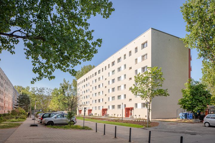 Sechsetagiger, heller, sanierter Plattenbau mit roten Hauseingängen und von vielen, grünen Bäumen umgeben