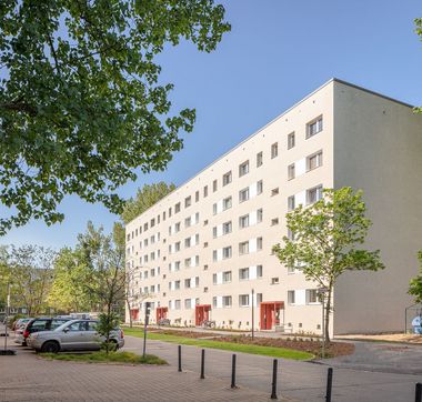 Sechsetagiger, heller, sanierter Plattenbau mit roten Hauseingängen und von vielen, grünen Bäumen umgeben