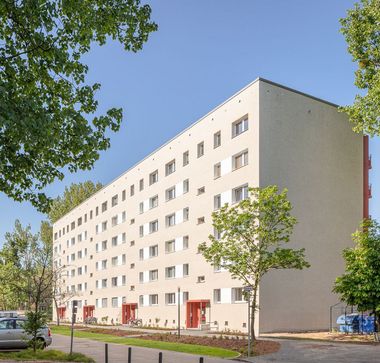 Sechsetagiger, heller, sanierter Plattenbau mit roten Hauseingängen und von vielen, grünen Bäumen umgeben