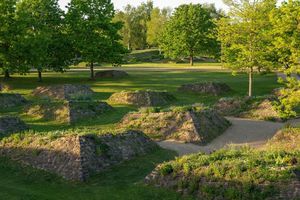 Es sind mehrere begrünte Hügel aus Stein in einem Park mit grüner Wiese und Bäume zu sehen.