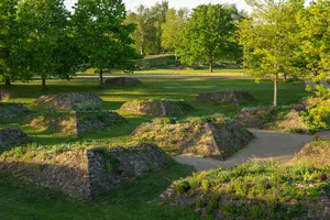 Es sind mehrere begrünte Hügel aus Stein in einem Park mit grüner Wiese und Bäume zu sehen.