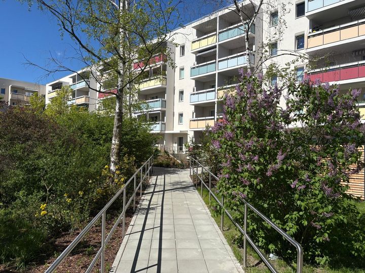 Sanierungsvorhaben erfolgreich abgeschlossen Modernisierte Wohngebäude mit neuen Balkonen, barrierefreiem Weg und begrünten Außenanlagen nach abgeschlossener Sanierung