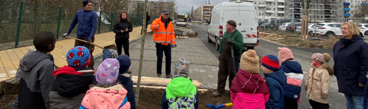 Mehrere Kinder die am Straßenrand einen Baum einpflanzen.