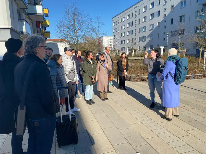 Eine im halbkreisstehende Menschengruppe vor einem Wohngebäude. 