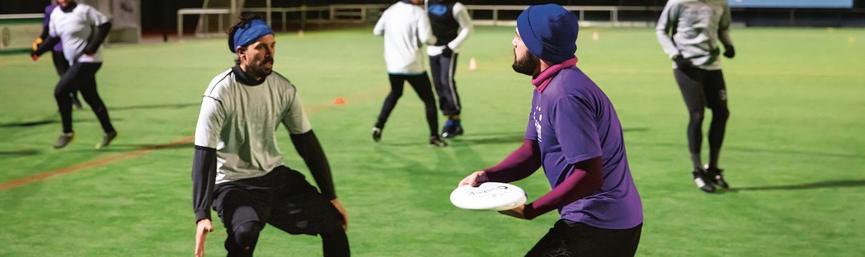 Junge Menschen spielen auf dem grünen Rasen eines Sportplatzes mit einer Frisbee-Scheibe. 