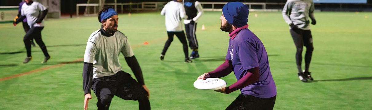 Junge Menschen spielen auf dem grünen Rasen eines Sportplatzes mit einer Frisbee-Scheibe. 