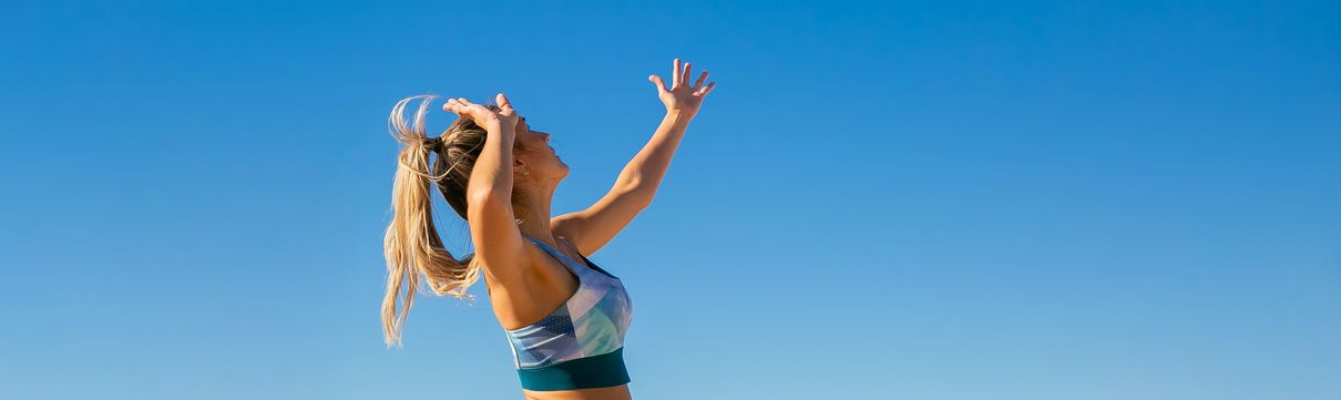 Auf dem Bild ist eine Frau im Sportoutfit zu sehen, die vor einem blauen Himmel zum Schlag auf einen Volleyball ausholt.