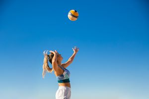 Auf dem Bild ist eine Frau im Sportoutfit zu sehen, die vor einem blauen Himmel zum Schlag auf einen Volleyball ausholt.