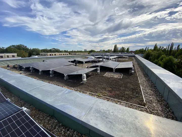 Solaranlage auf einem Flachdach mit mehreren Photovoltaikmodulen unter einem bewölkten Himmel.