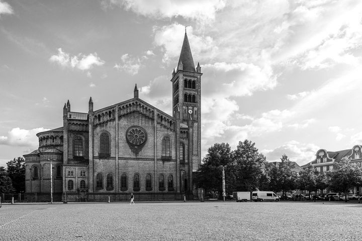 Schwarz-Weiß-Foto einer düster wirkenden großen Kirche, die am Ende eines großen Kopfsteinpflaster-Platzes steht