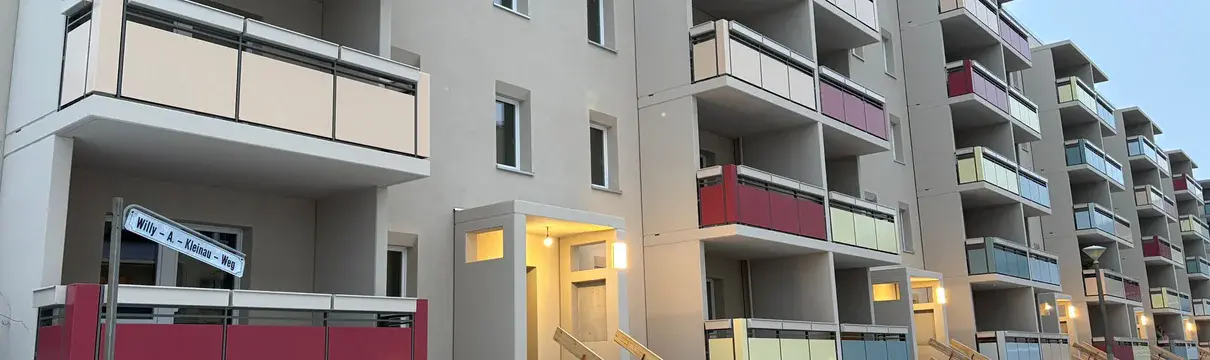 Sanierter Wohnblock im Willy-A.-Kleinau-Weg im Winter mit neuen Balkonen und farbigen Brüstungen; Eingangsbereiche beleuchtet, Bauarbeiten im Außenbereich noch nicht abgeschlossen.