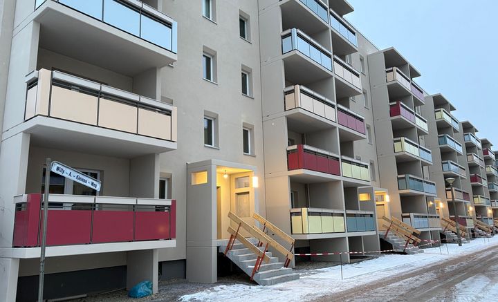 Sanierter Wohnblock im Willy-A.-Kleinau-Weg im Winter mit neuen Balkonen und farbigen Brüstungen; Eingangsbereiche beleuchtet, Bauarbeiten im Außenbereich noch nicht abgeschlossen.