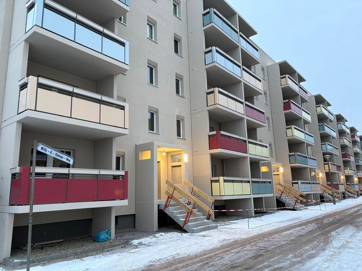 Sanierter Wohnblock im Willy-A.-Kleinau-Weg im Winter mit neuen Balkonen und farbigen Brüstungen; Eingangsbereiche beleuchtet, Bauarbeiten im Außenbereich noch nicht abgeschlossen.