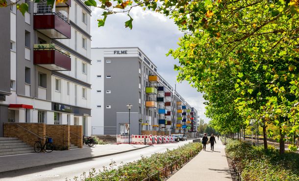 sanierte Plattenbauten mit bunten Balkonen und begrünter Mittelstreifen in der Konrad-Wolf Allee