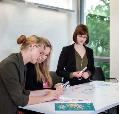 mehrere Personen stehen an einem Tisch und erarbeiten etwas