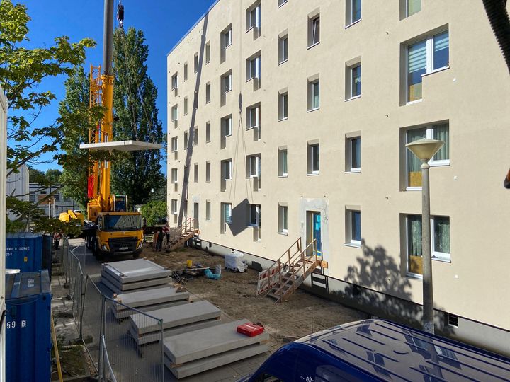 Ein Kran der neben einem Gebäude Betonteile in die Luft hebt.