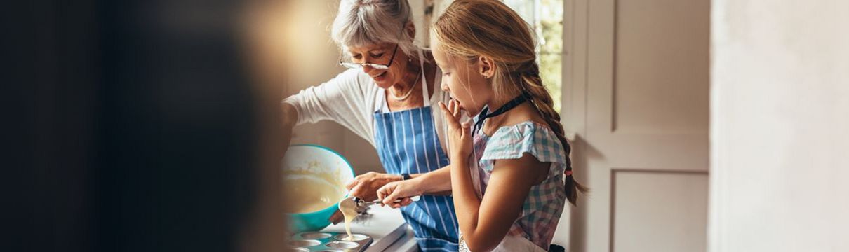 Eine ältere Dame bäckt mit Ihrer Enkelin Muffins und füllt Teig in die Förmchen