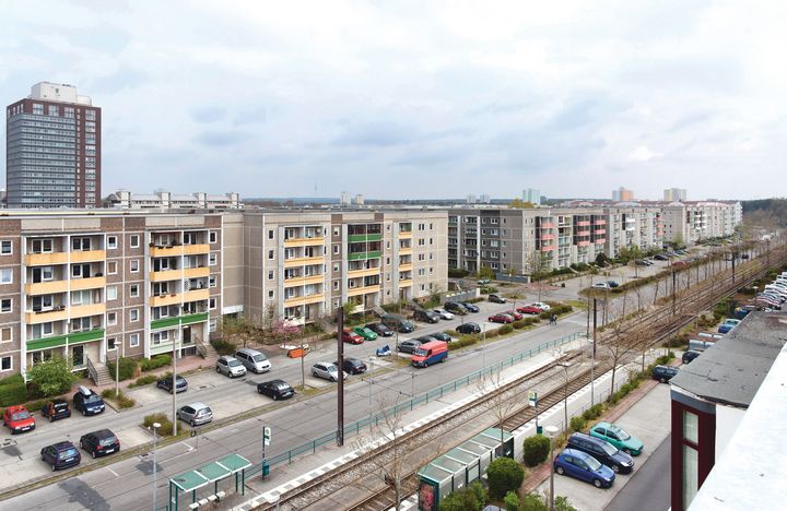 Eine lange Straße mit vielen Autos vor zahlreichen Wohnhäusern.