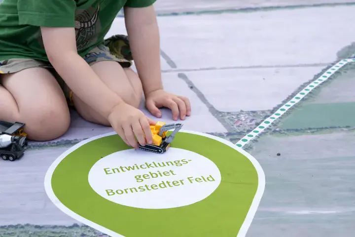Kind spielt mit einem Spielzeugbagger auf einer Bodenkarte des Entwicklungsgebiets Bornstedter Feld in Potsdam.