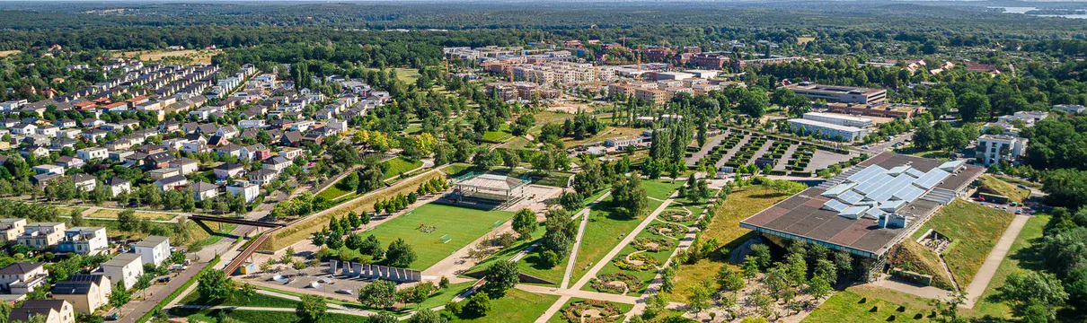 Luftaufnahme eines grünen Stadtquartiers mit Wohngebieten, Parkanlagen, Wegen und Gebäuden.