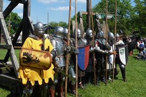Zu sehen sind als Ritter verkleidete menschen in Rüstungen mit Schilden und Speeren in den Händen vor sommerlicher Kulisse.