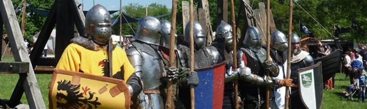 Zu sehen sind als Ritter verkleidete menschen in Rüstungen mit Schilden und Speeren in den Händen vor sommerlicher Kulisse.