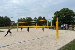 Zu sehen sind Männer und Frauen, die auf einem Sandfeld mit gelbem Netz Beachvolleyball spielen.